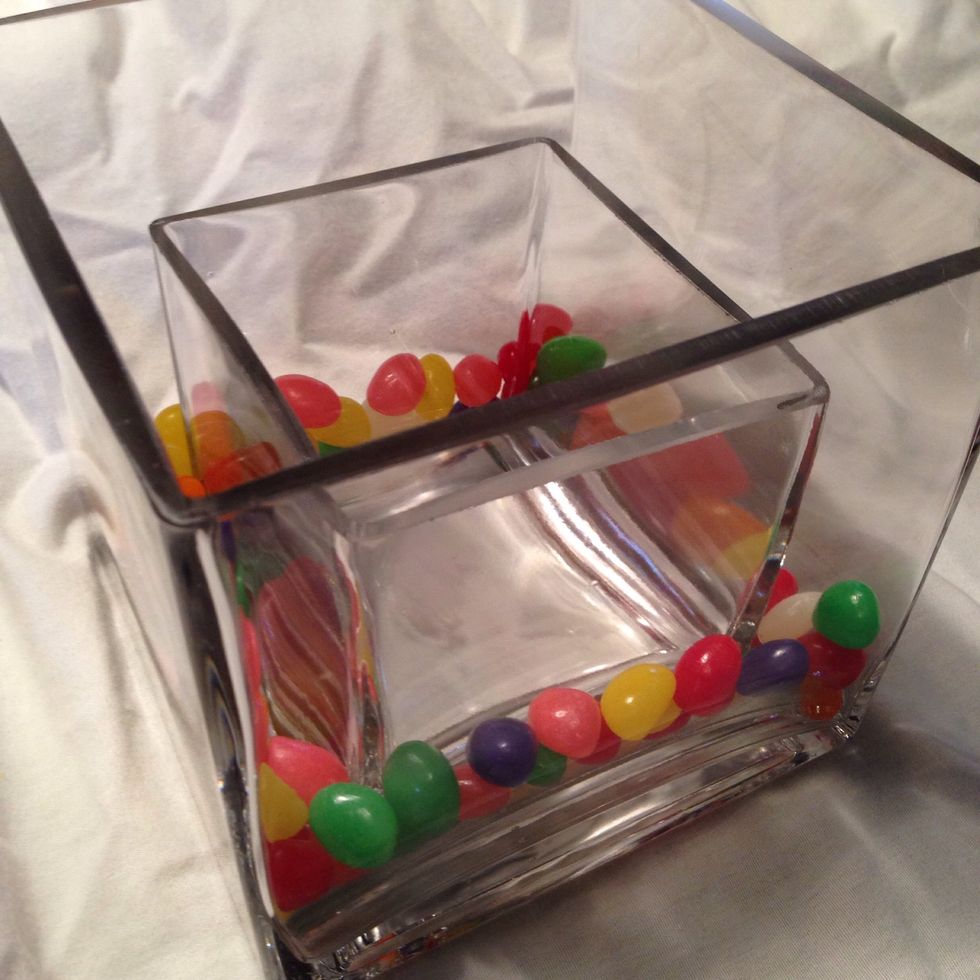 Pour jelly beans around the outside of the smaller vase. If you are up for it you can certainly use one single color of jellybeans. I removed the black ones. Fill the glass evenly about half way.