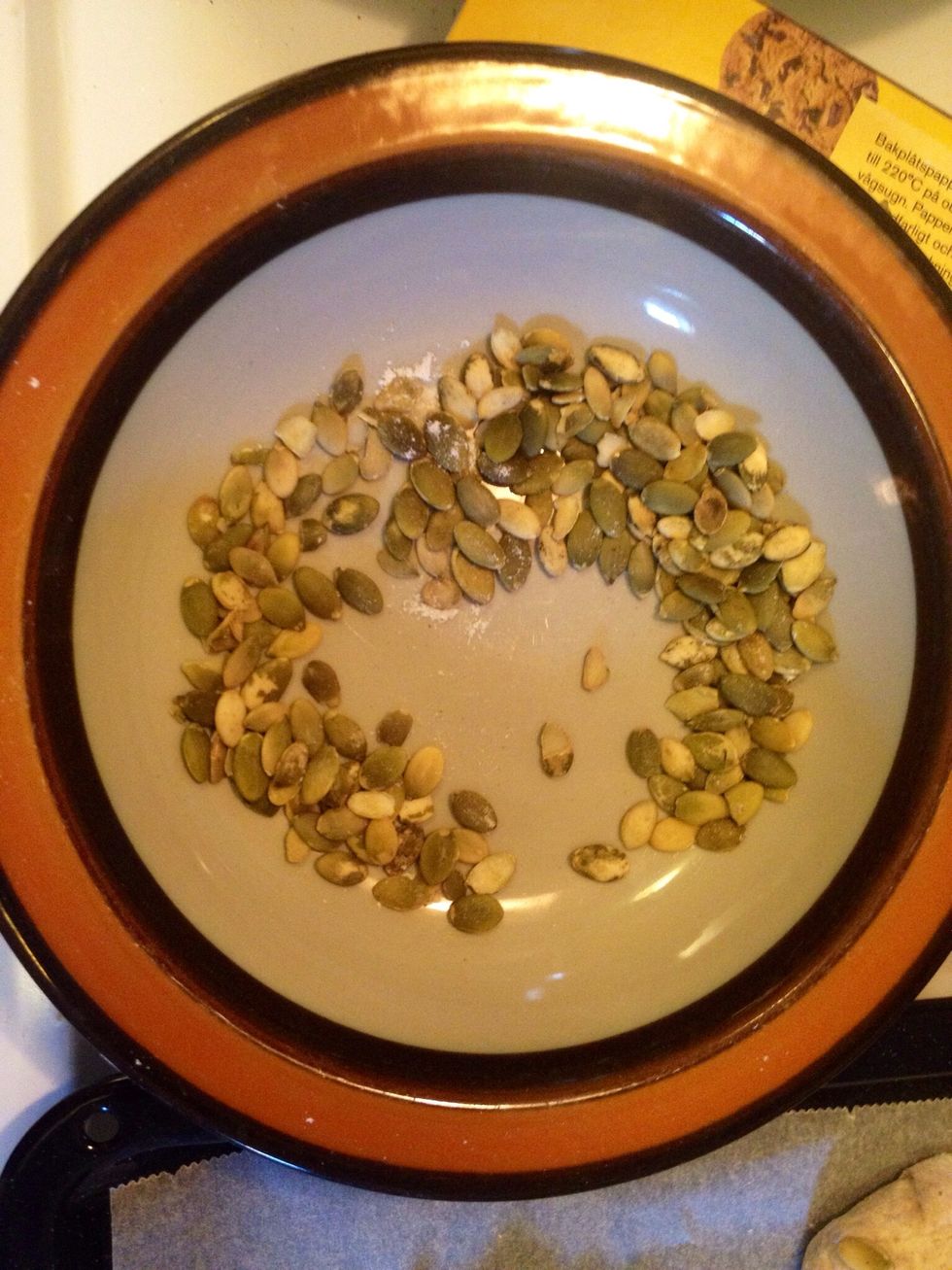 Pour pumpkin seeds into a plate to dip the cut ends of the breakfast buns into.