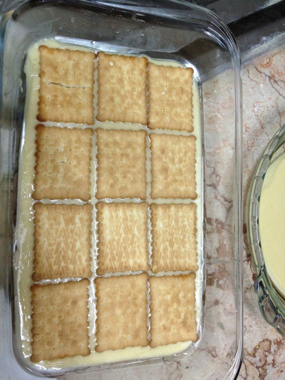 Prepare the cake mix and pour half of it in a greased tray. Then, arrange a layer of biscuits on the mix