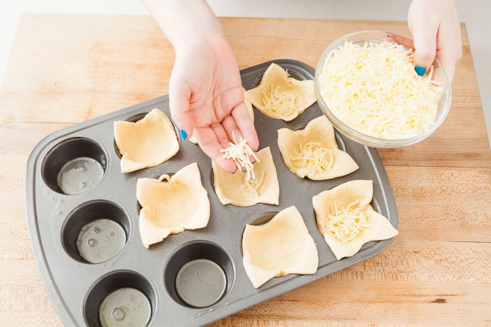Press your dough into each muffin cup. Sprinkle some cheese into each cup. 