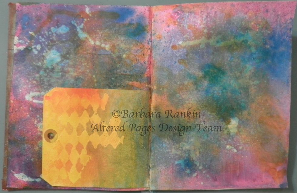 Protect both pages, spray both sides of tag with the DecoArt Shimmer Yellow and Orange Misters, pick up some of the DecoArt Shimmer Turquoise Mister with a baby wipe and add to tag.