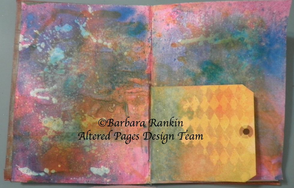 Protect tag and spray both pages with the DecoArt Shimmer Turquoise Mister, Shimmer Yellow Mister, and Orange Misters. Spray water over all and let each color move around the page. Dab excess water