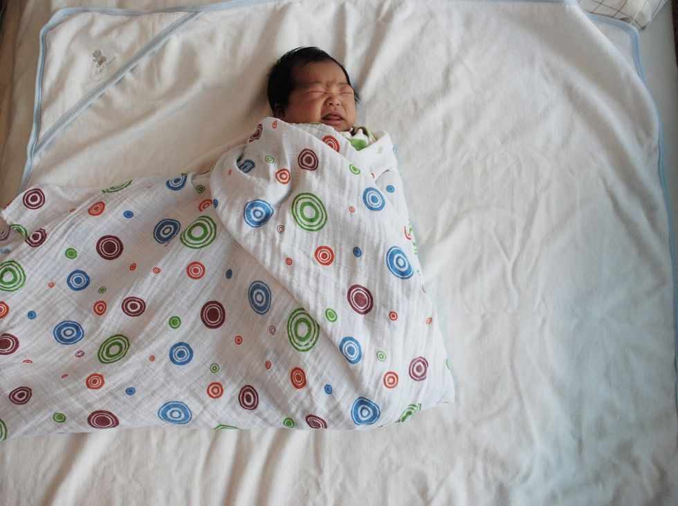 Pull one side of the blanket across the baby's chest. Tuck under opposite Arm. Fold bottom blanket over feet and baby's shoulders.