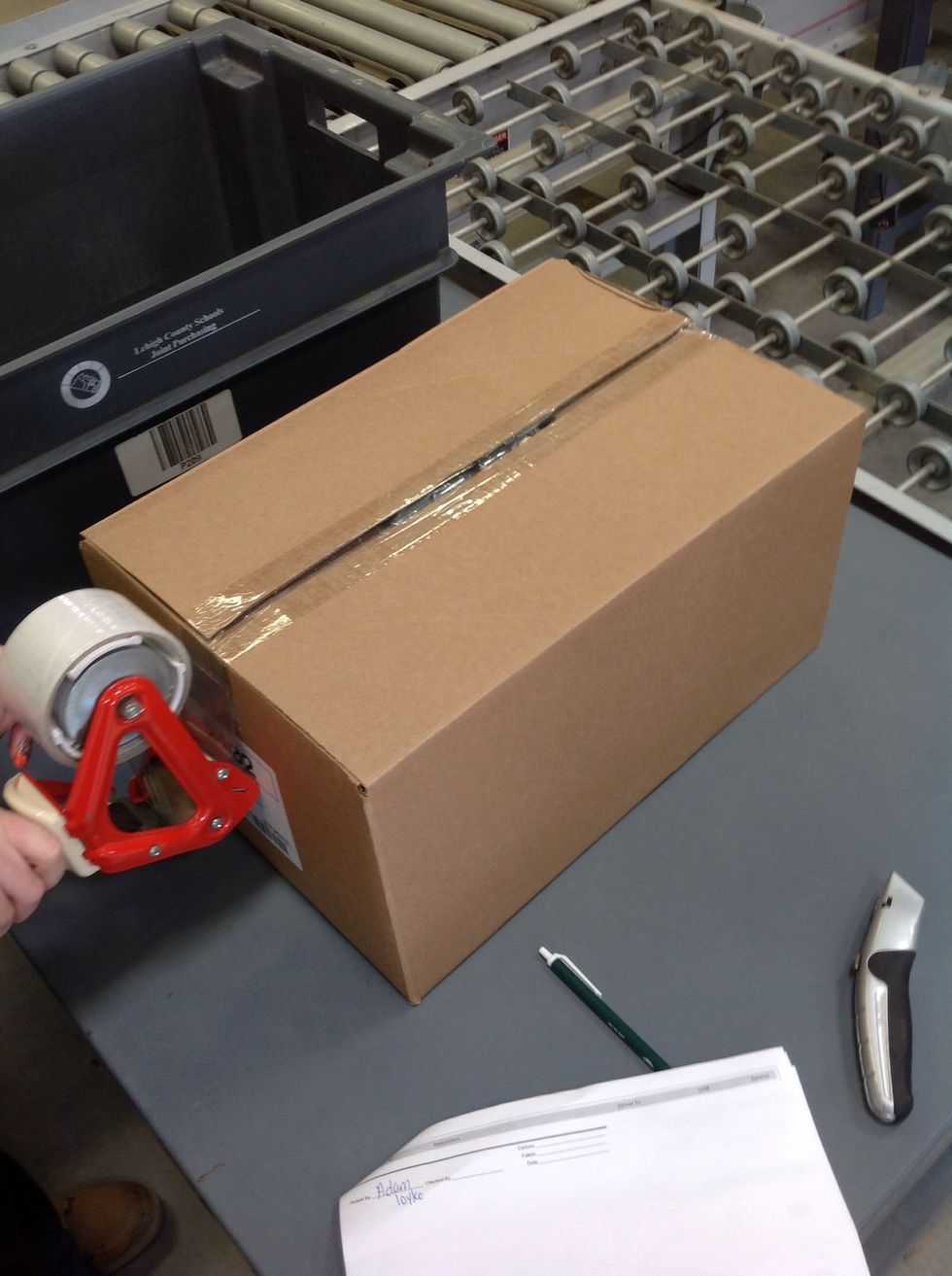 Pull the tape gun over the edge of the carton and secure it to the side of the box. Cut the tape by applying pressure and tilting slightly forward so that the teeth of the tape gun cut the tape.