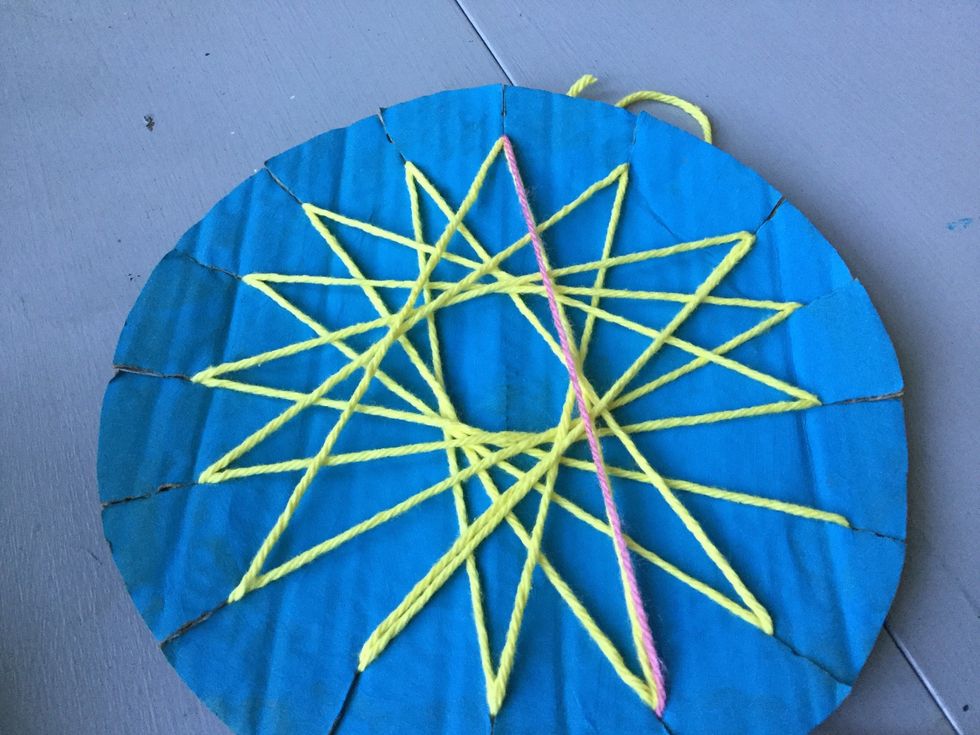 Pull the yarn through one of the slits and pull across the cardboard to the slit diagonal from the first slit. Follow the same pattern as you did with the first color of yarn