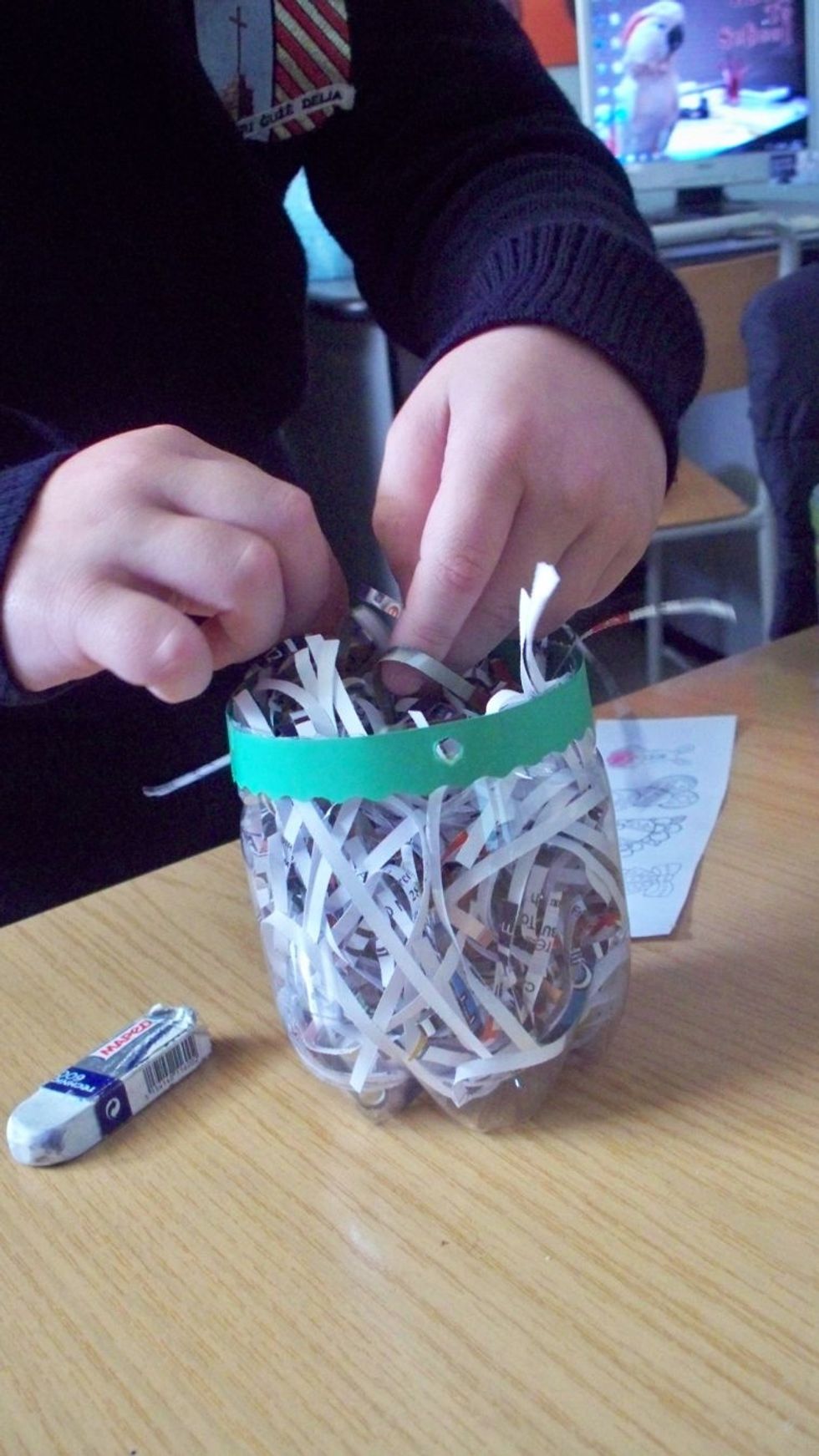 Punch 2 holes on opposite sides of the bottle then insert some shredded magazine paper into the bottle.