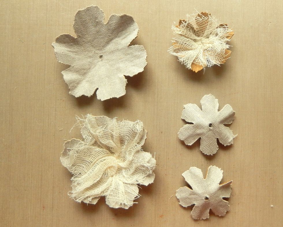 Punch a hole in the centre of each flower layer. Add an uneven piece of gauze onto one of the large fabric covered flowers and the small uncovered flower.