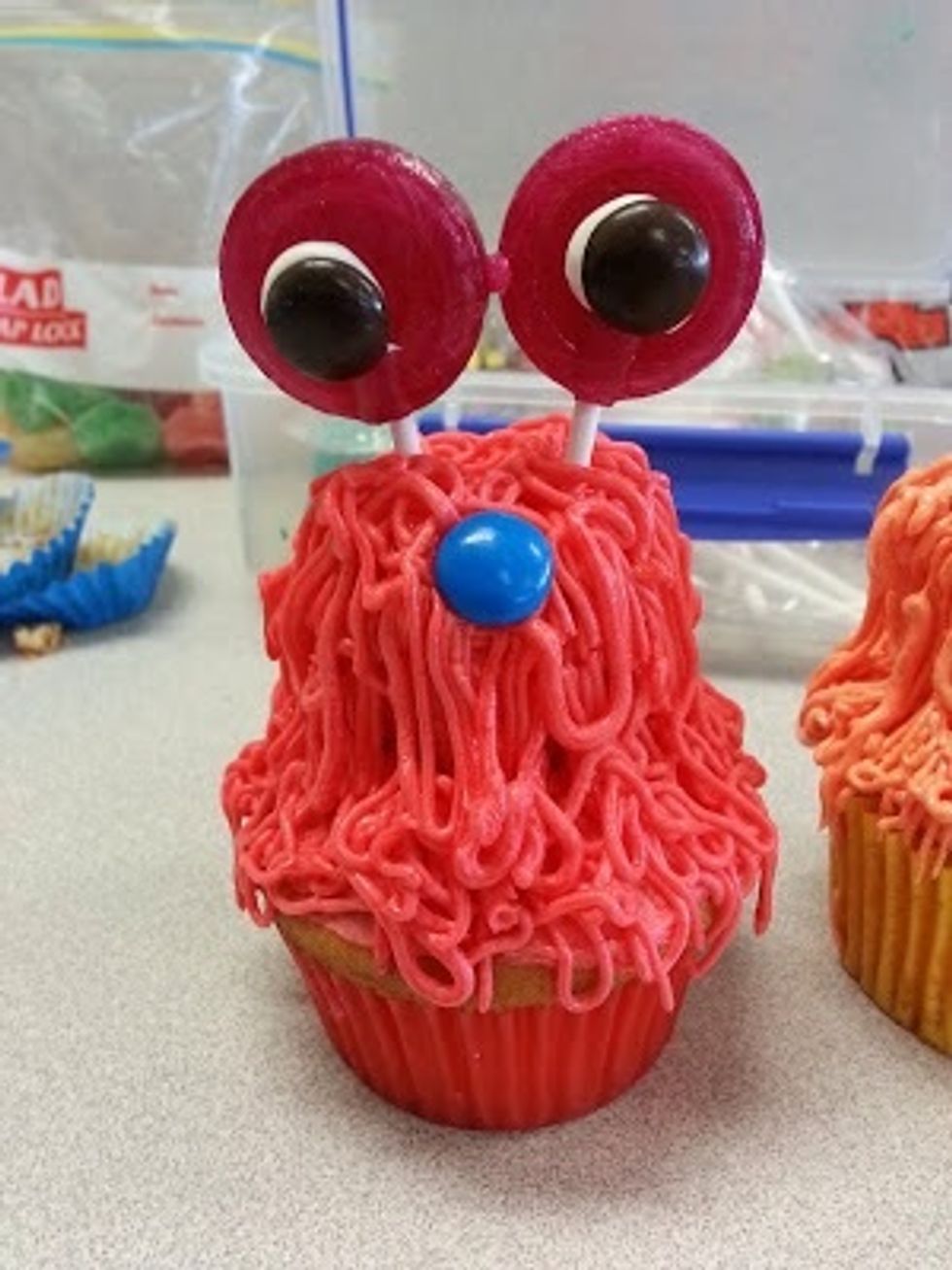 Push two lollipops into the cupcake to create the eyes. Use a colored m&m for the nose