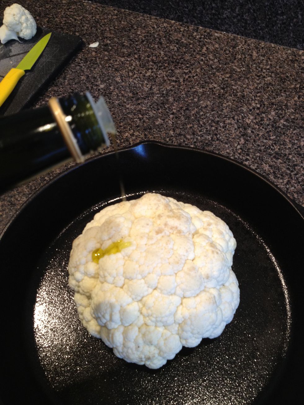 Put cauliflower into oven proof pan (cast iron is preferrable) and pour olive oil onto cauliflower and rub over entire cauliflower until coated.