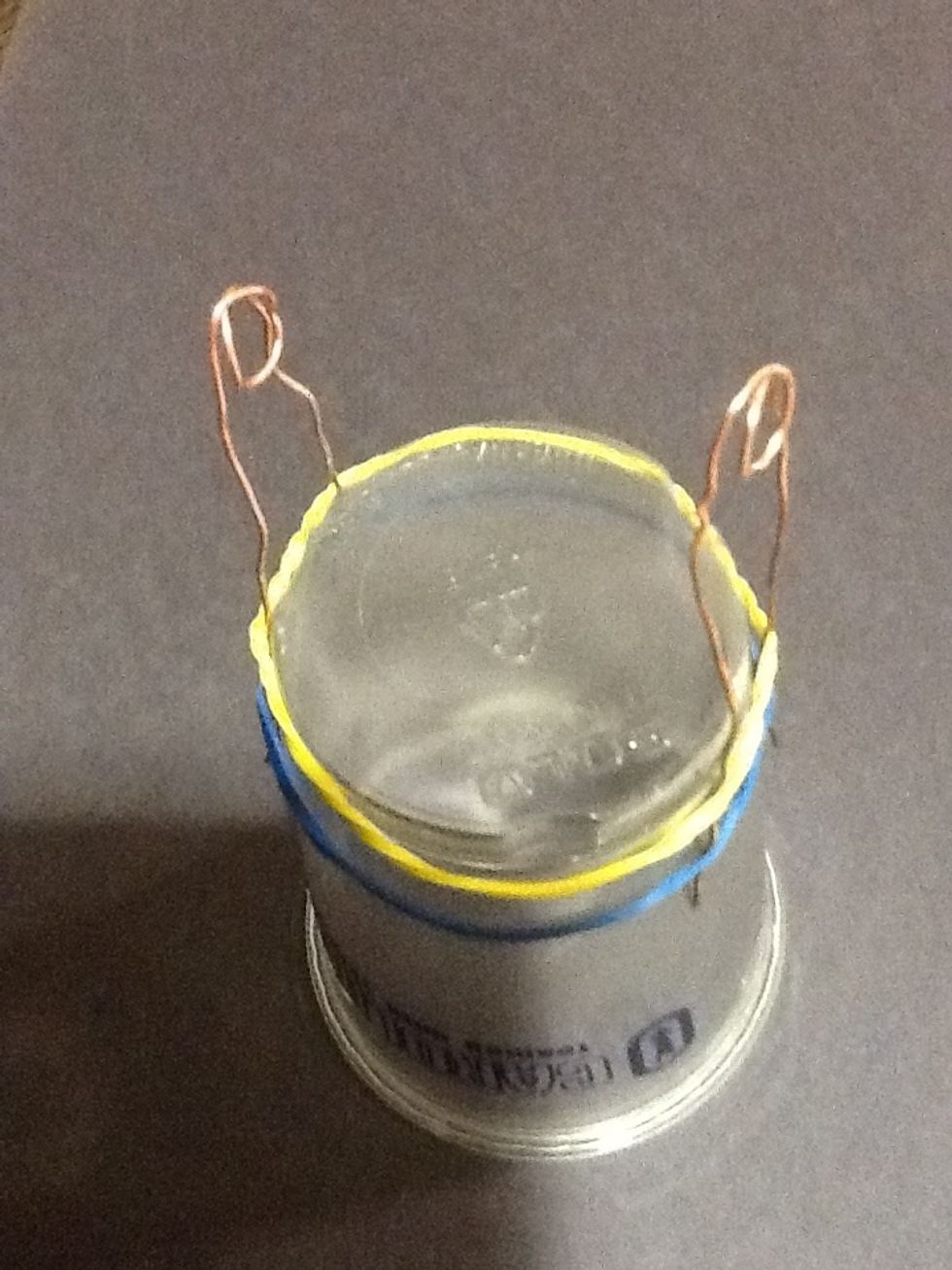 Put each rubber band over the cup. Then put both bare copper wires thought both of the rubber bands on either side.