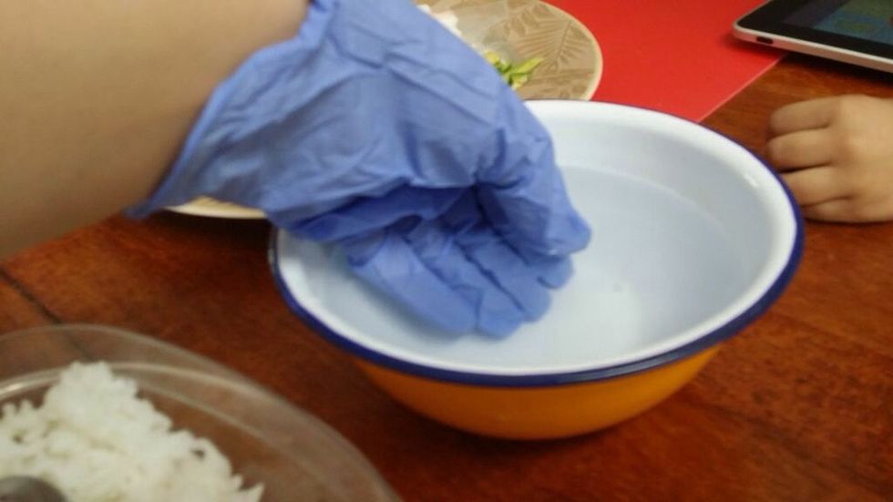 Put on a pair of rubber gloves and fill your small bowl with cold water. Dip your covered hands in the water. This will help you work with the rice without it constantly sticking to your hands.