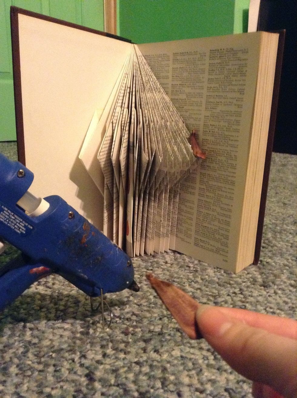 Put some hot glue on the back of the pine cone piece and glue it tothe bottom of your roof. Go all the way across the row. When you filled that up, make a row above it and continue.