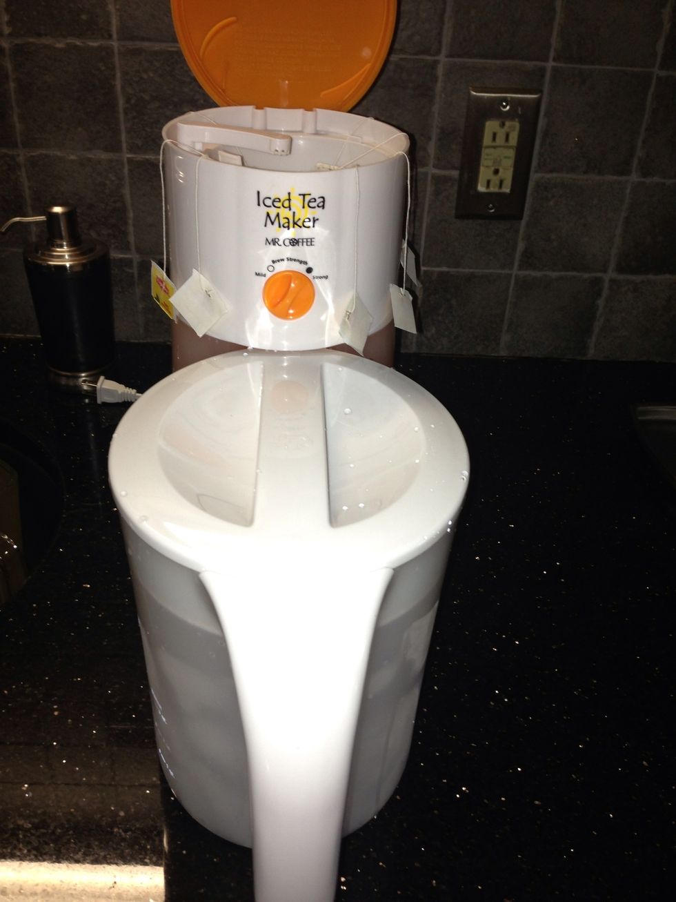 Put the cover on the iced tea pitcher and position the pitcher so that it lines up underneath the spout of the iced tea maker.