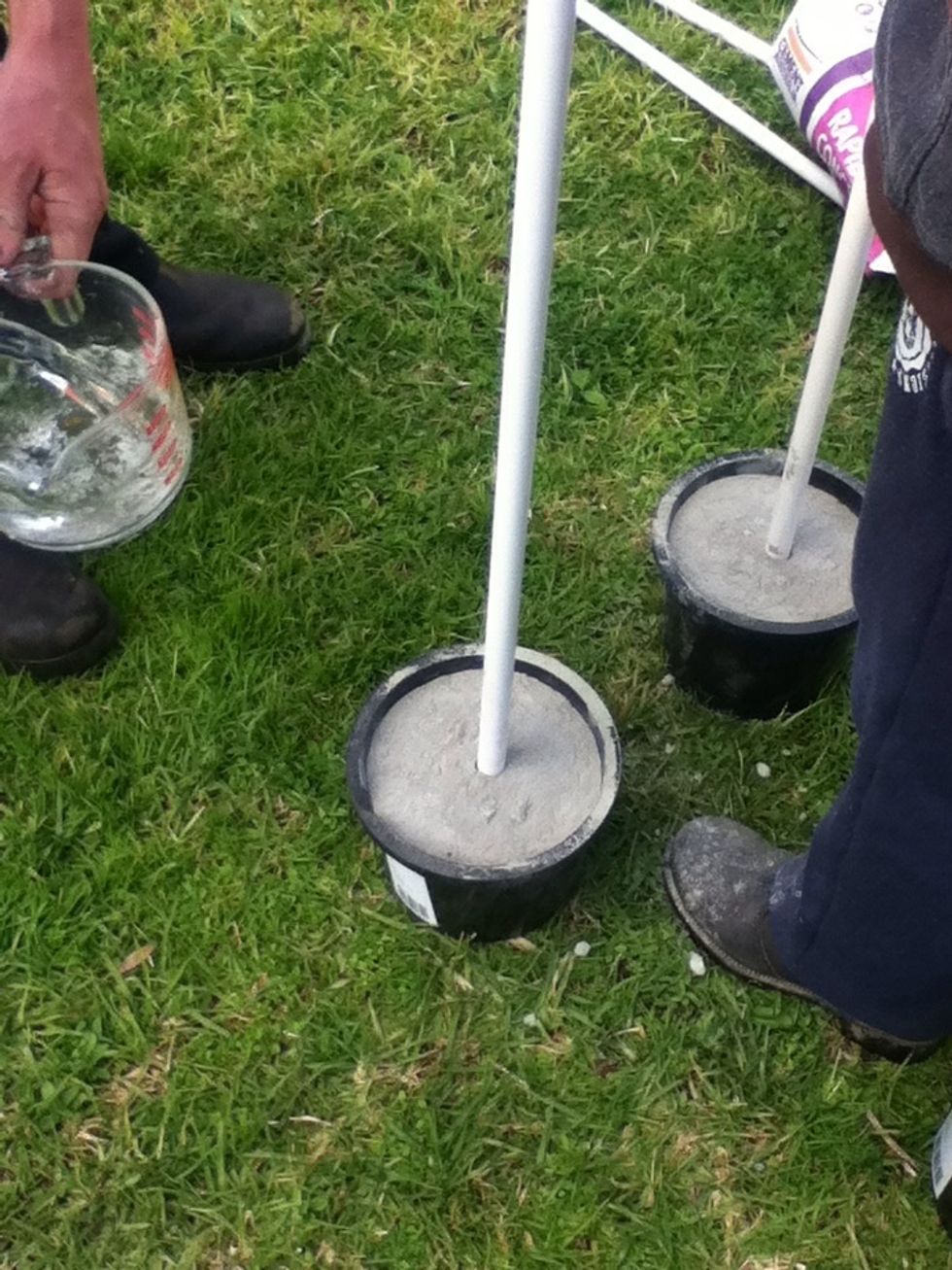 Put the poles in the buckets vertically strait and put the cement in the bucket and around the pole.