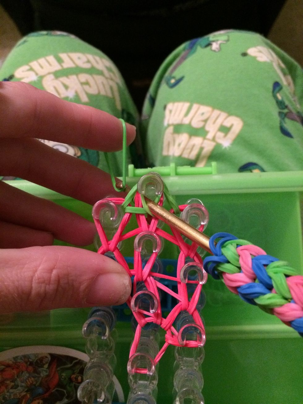 Put your hook into the peg and go out the side. Put 1 green band on the end of the hook. Hold onto one end of the band and pull the other end with the hook.
