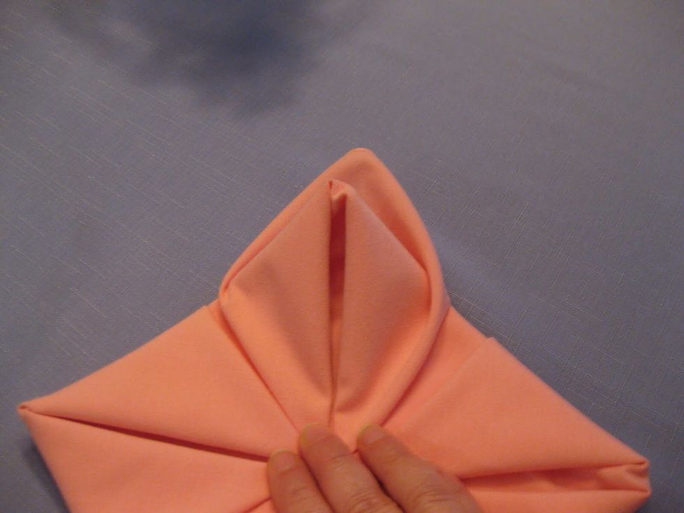 Reach behind the corner of the napkin and pull the material from behind up and around