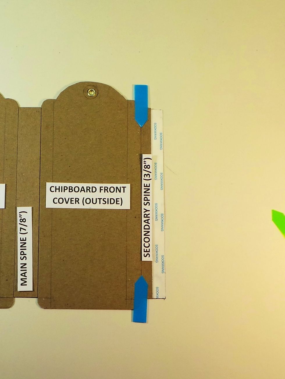 Remove backing from center Scor-tape strip on Tyvek and butt one of the secondary (3/8") spines against the chipboard tag (blue arrows) . The outside of chipboard tag should be facing up.