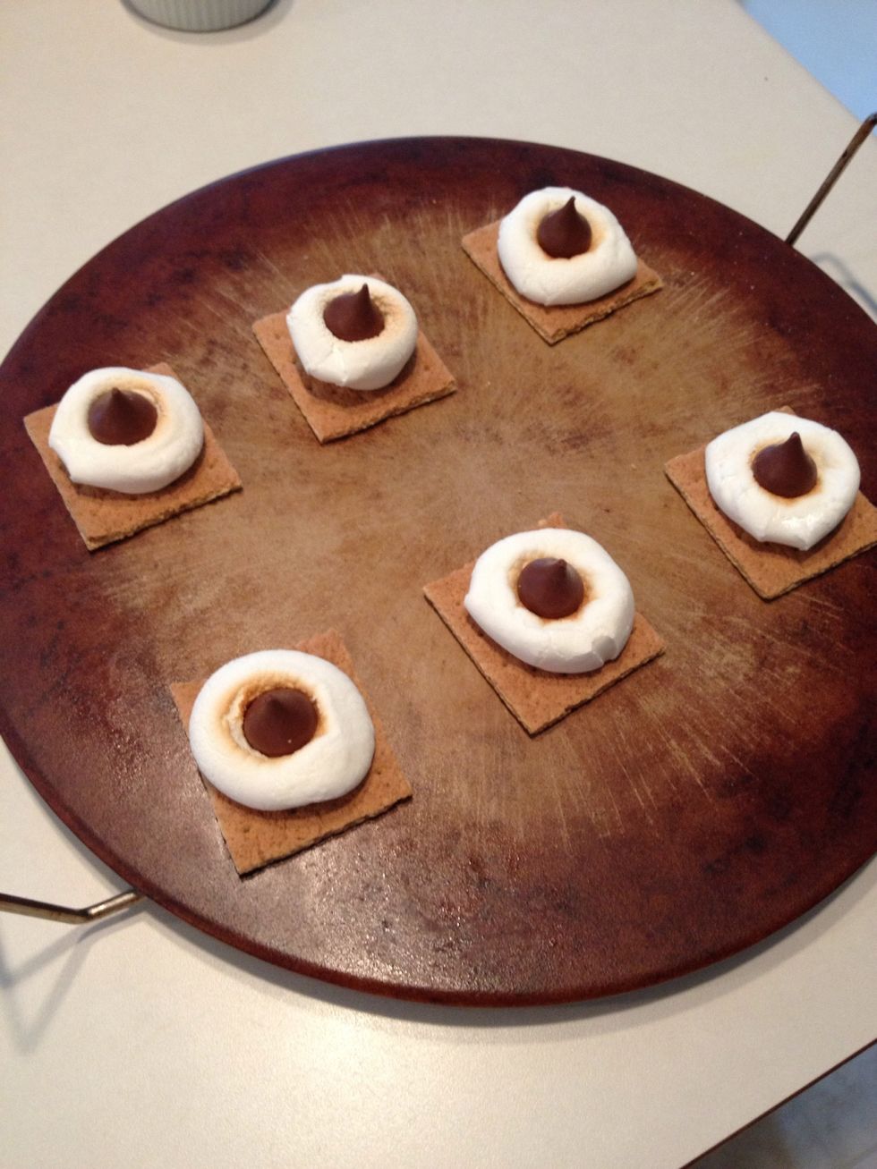 Remove from oven and place one Hershey kiss in the middle of each marshmallow, pressing down to make it stay.