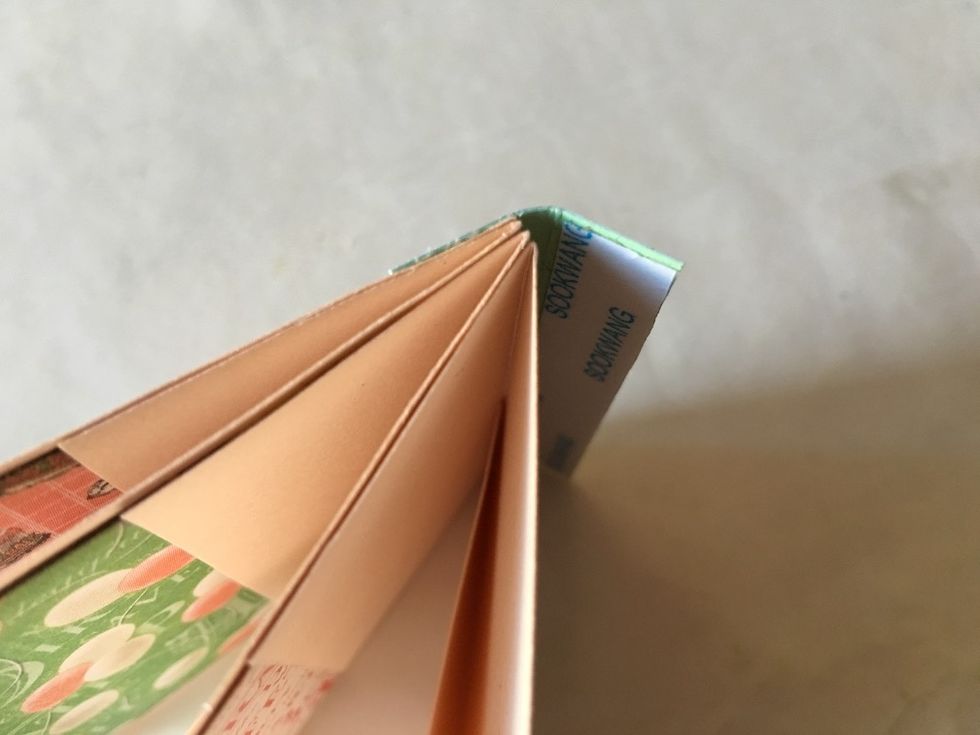 Remove one of the tape backings. Fold your spine over the folded edges of your pages and attach the first flap of your spine, as shown.