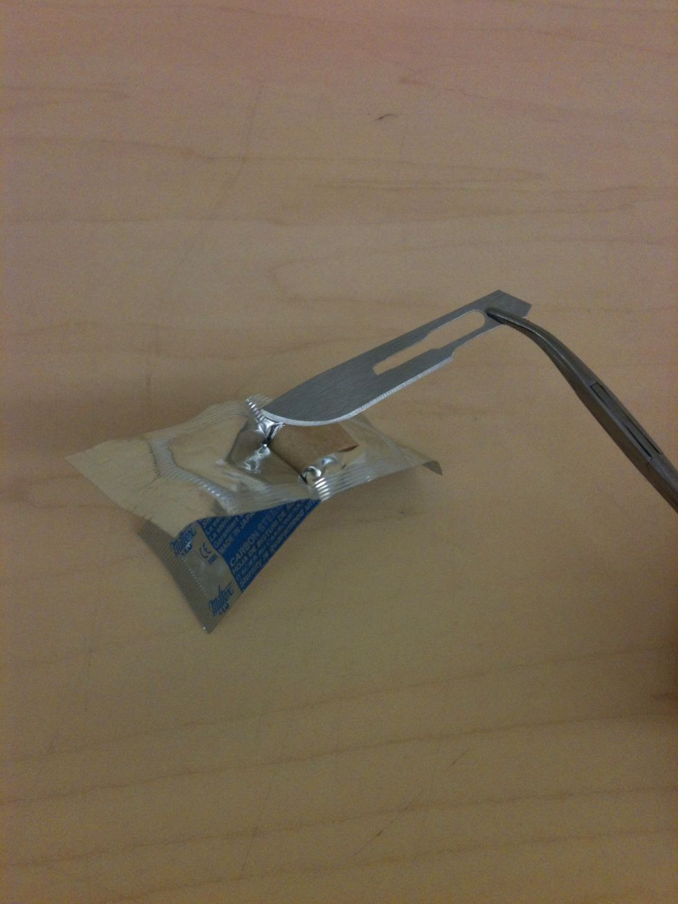 Remove the blade from the wrapper using a pair of hemostats. Never handle the scalpel blade with your fingers!