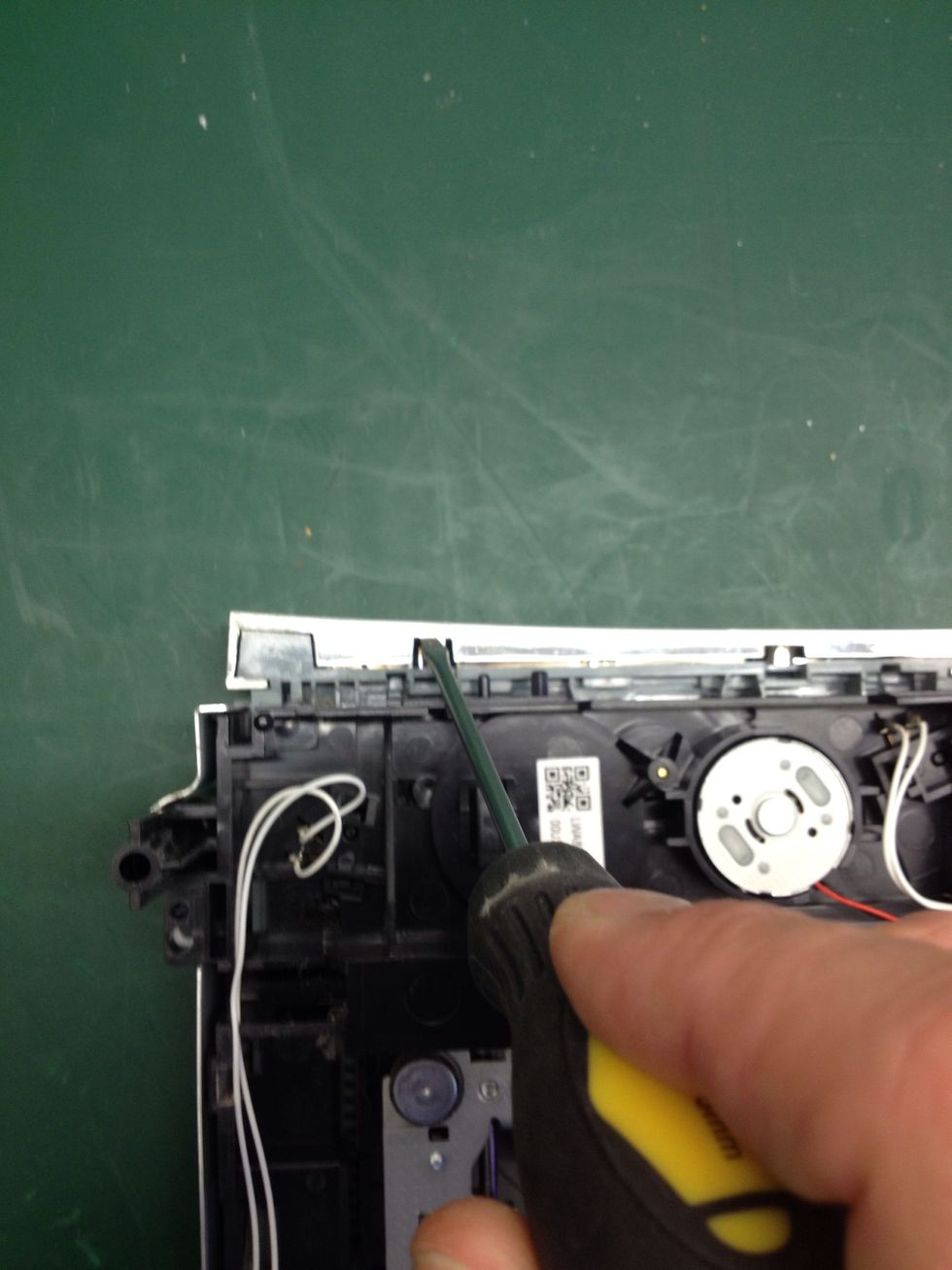 Remove the drawer bezel using the small flathead screwdriver to push down gently on the tabs shown.