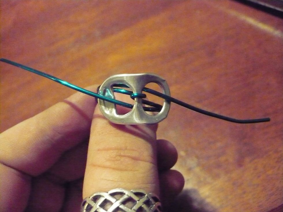 Remove the ring from the mandrel. Slide the ends of the wire up through the tab from opposite sides. Note how the wire from the left comes up though the right.