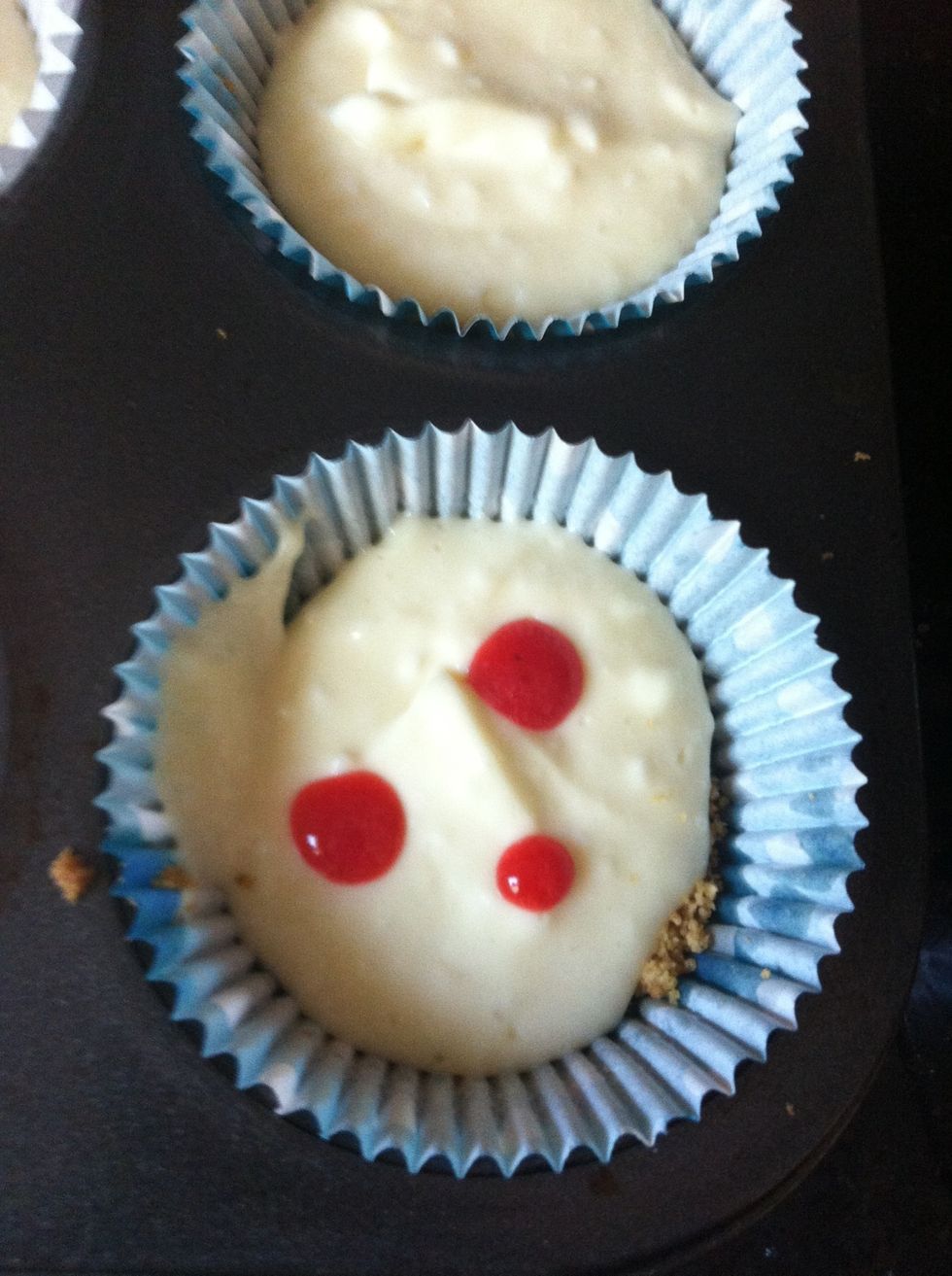 Retrieve the raspberry 'syrup' and use a spoon to drop about 3-4 drops onto each cupcake.