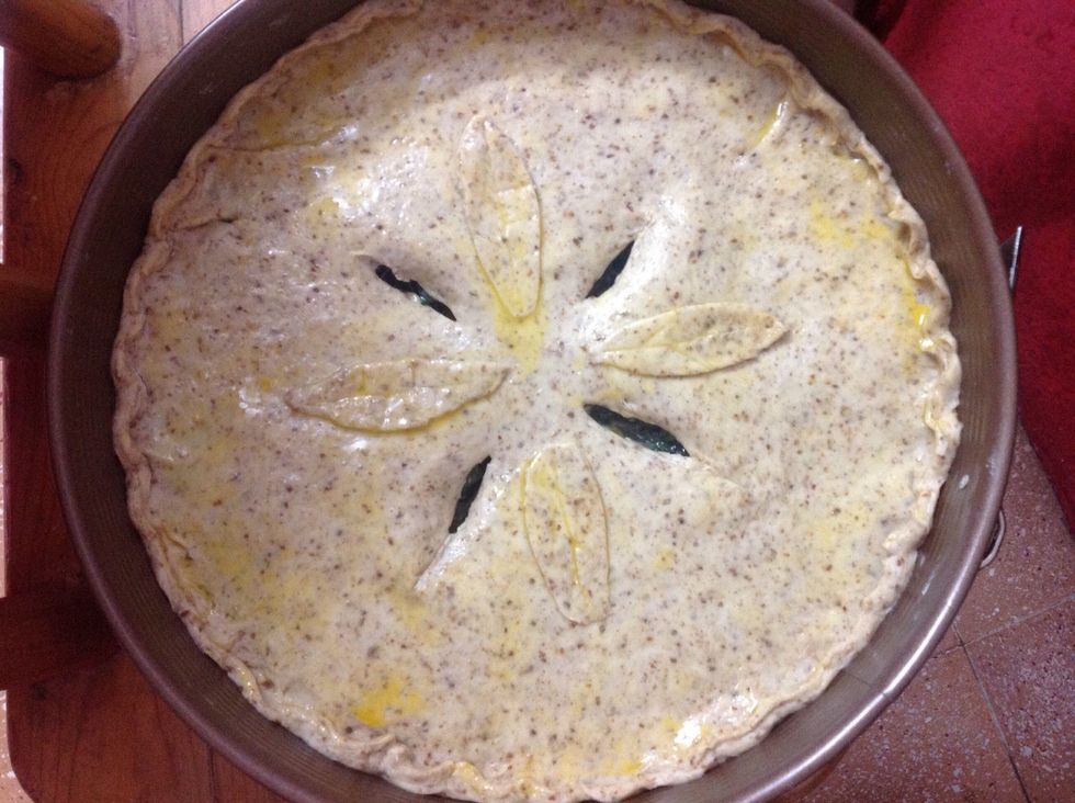 Roll out 2 balls of dough to cover the filling and close the rim well to avoid spilling when the Pascualina cooks. Brush with egg yolk and add decorations with left over dough. Cut slots in the middle