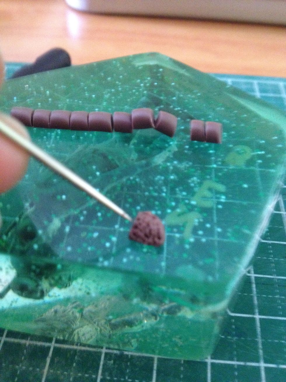Roll the brown clay out and cut the snake into pieces. Take each piece and start dotting it, creating the soil texture.