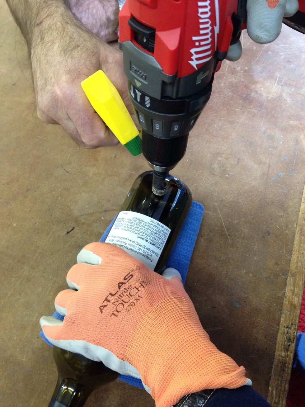Roll the towel in from both ends to make a cradle. Position the bottle on the rolled towel for stability. One person sprays water (lubrication) while the other person drills down.