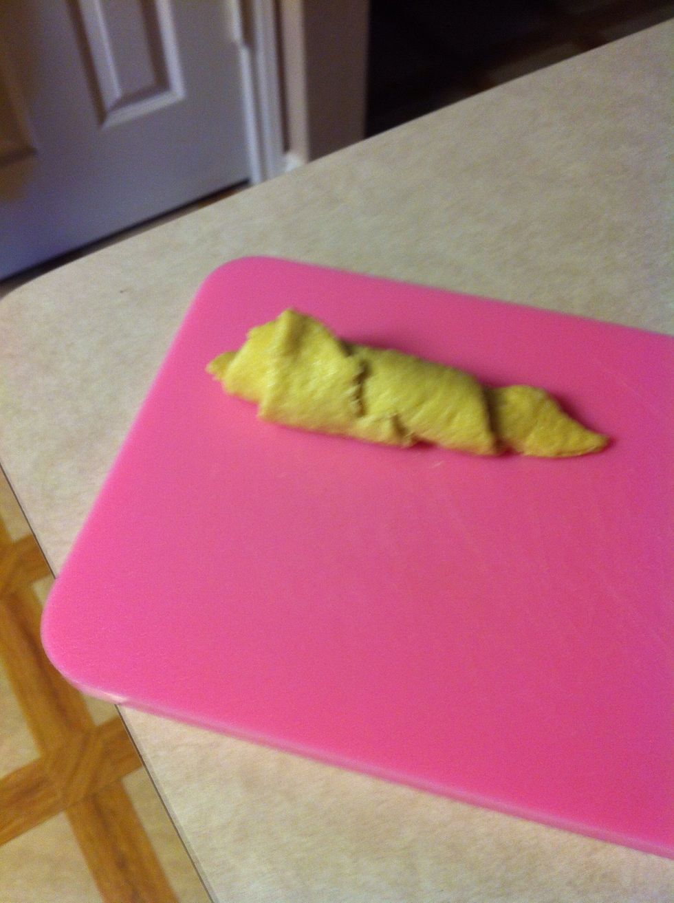 Roll up one of the crescent roll triangles and place in on the cutting board.