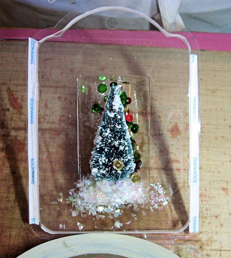 Run a line of 1/4" Scor-Tape all the way around the outside edge of the packaging. This will keep the glitter from falling out. Add Stampendous Shaved Ice, glitter, sequins and beads to the cavity.