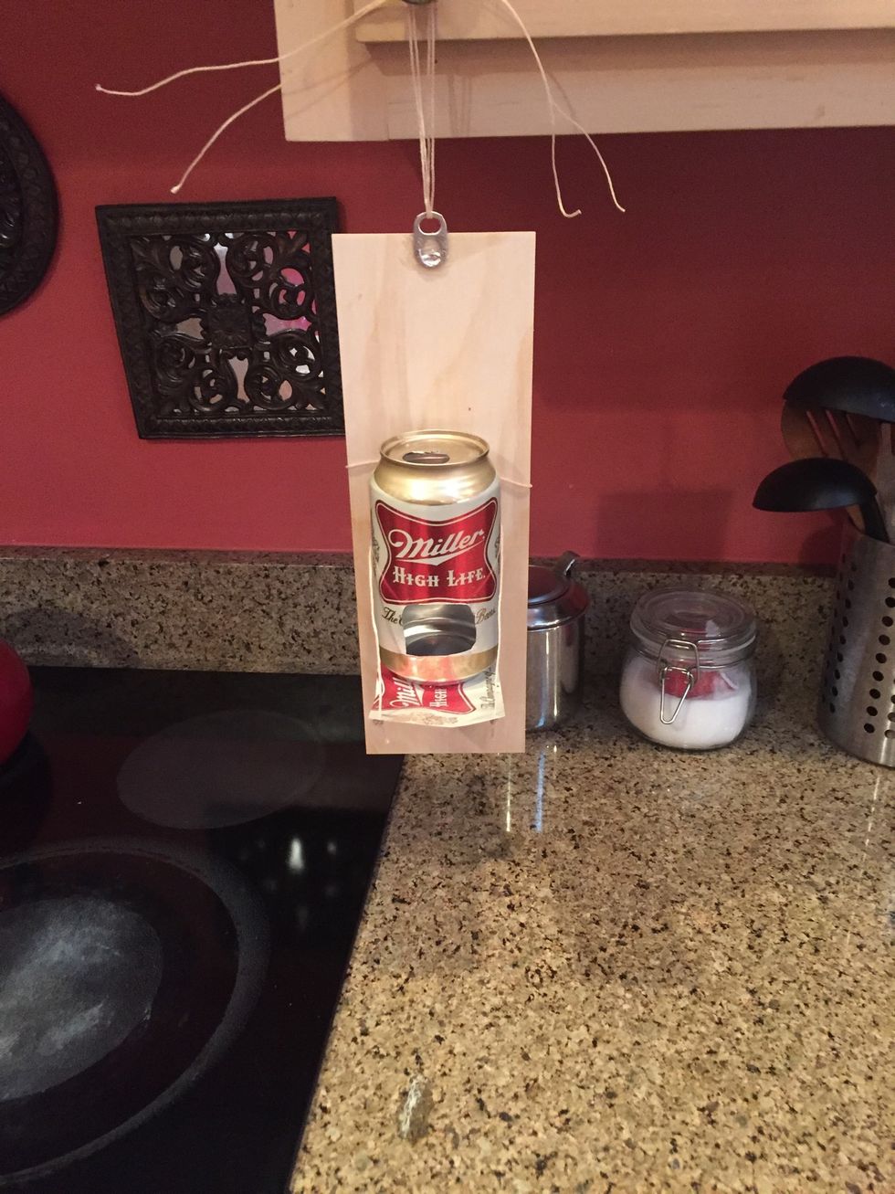 Run the string through the little can opener piece at the top of the piece of wood