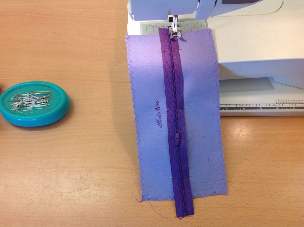 S\u00e4tt pressarfoten med kanten mot upph\u00f6jningen p\u00e5 dragkedjan. Sy hela v\u00e4gen ner. V\u00e4nd din bit och sy p\u00e5 andra sidan ocks\u00e5.