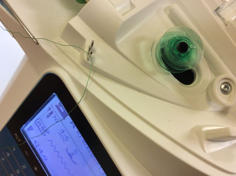 S\u00e4tt spolen p\u00e5 den svarta spolarmen, H:et ska vara ut\u00e5t. L\u00e4gg tr\u00e5den genom metallgafflen p\u00e5 maskinen.