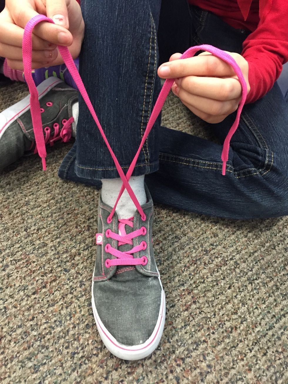 Second, holding a lace in each hand, cross them over one another.