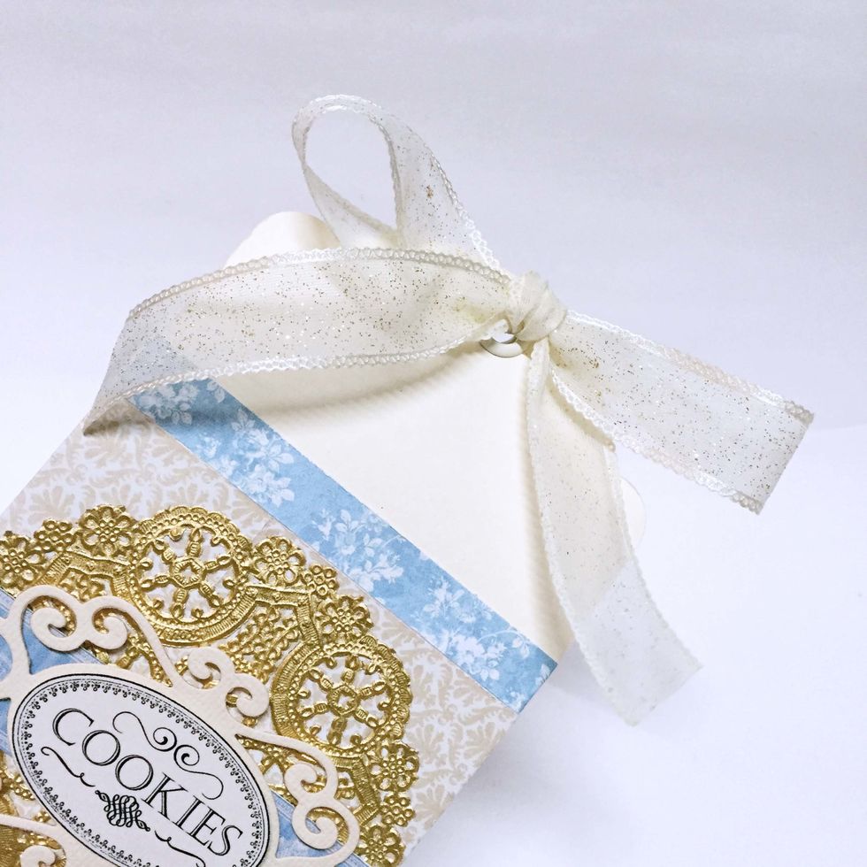 Secure the box by tying some ribbon over the grommets of the tags. This will complete the gift box.
