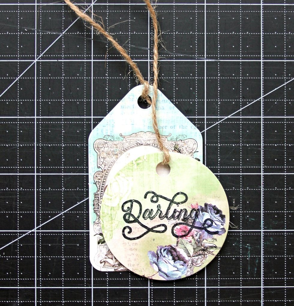 Select a rectangular and a circular tag from the Garden Fable Tags. Stamp \u201cDarling\u201d on one. Add twine to the top of each tag. Adhere tags together using dimensional foam adhesive.