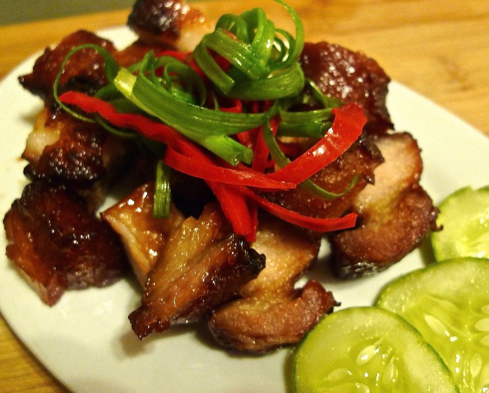 Serve the cut barbecue pork as a main dish on a serving plate garnish with sliced cucumbers, spring onions and red chillies.
