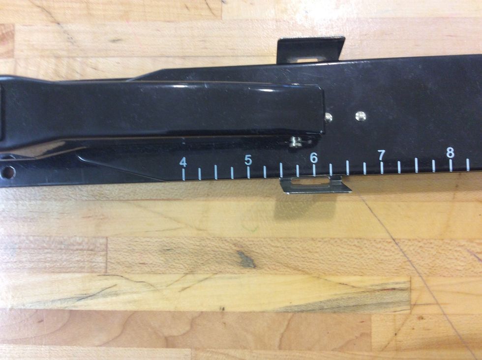 Set the silver metal measuring tab on the booklet stapler so that the side nearest to the front is lined up between the 5 & 6 marks (at five and a half).