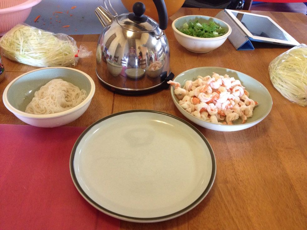 Set up assembly station with separate containers around a cutting board (working surface): rice paper wrappers, shrimp, rice noodles, lettuce, mint, basil, cilantro.