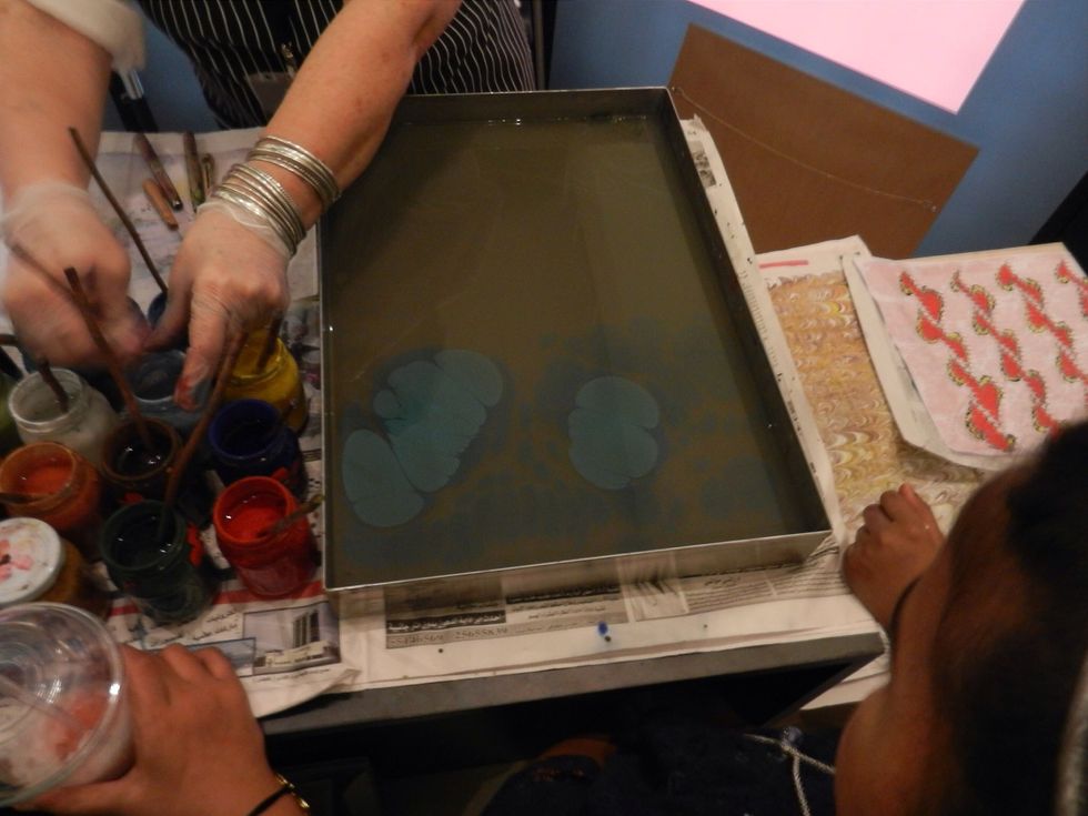 She starts adding paint, allowing it to spread out on the surface.
