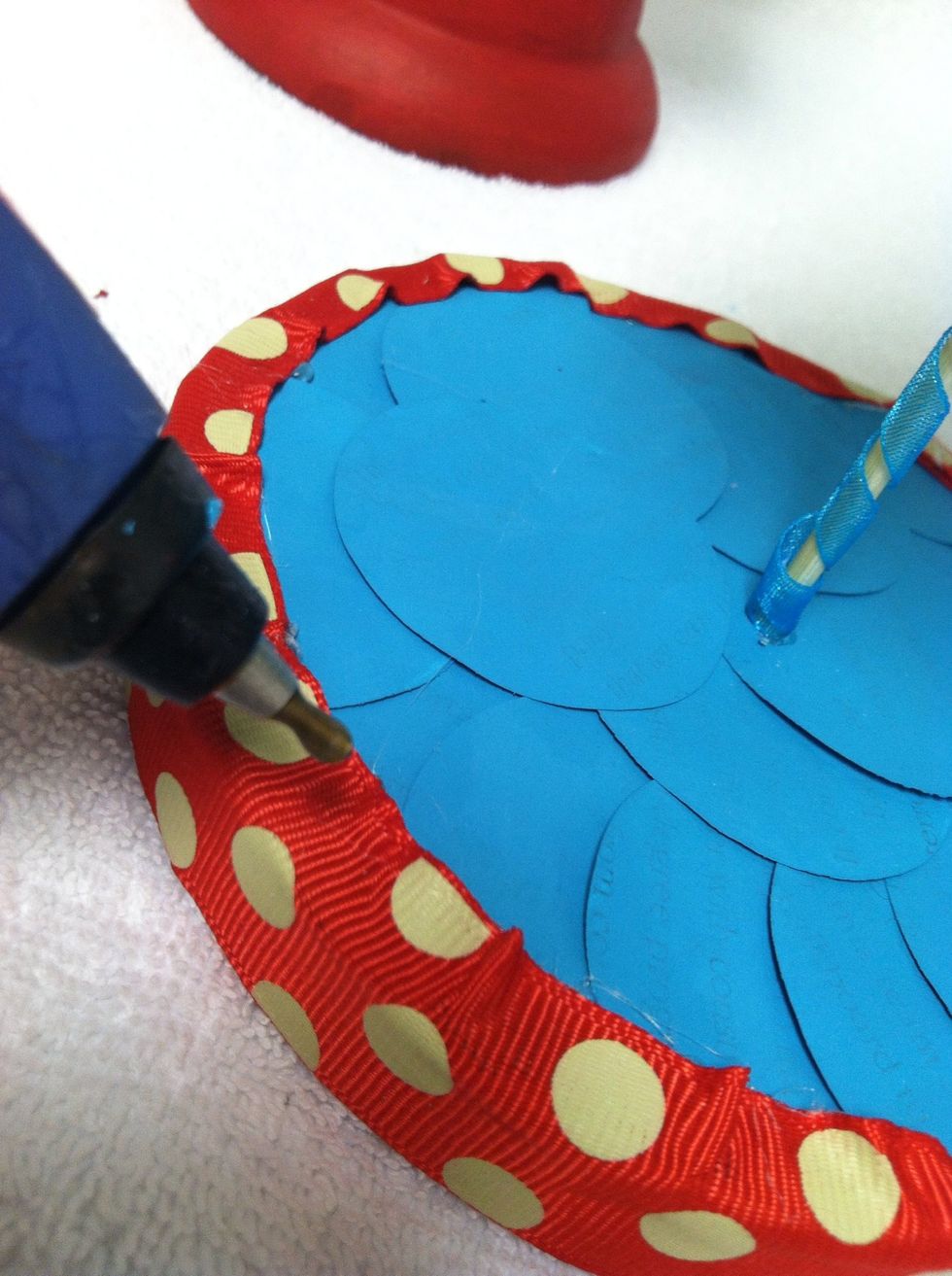 Since the ribbon is flush with the bottom, it will be taller than the base. Add another string of glue to the top of the base where you applied the circles then push the ribbon down.