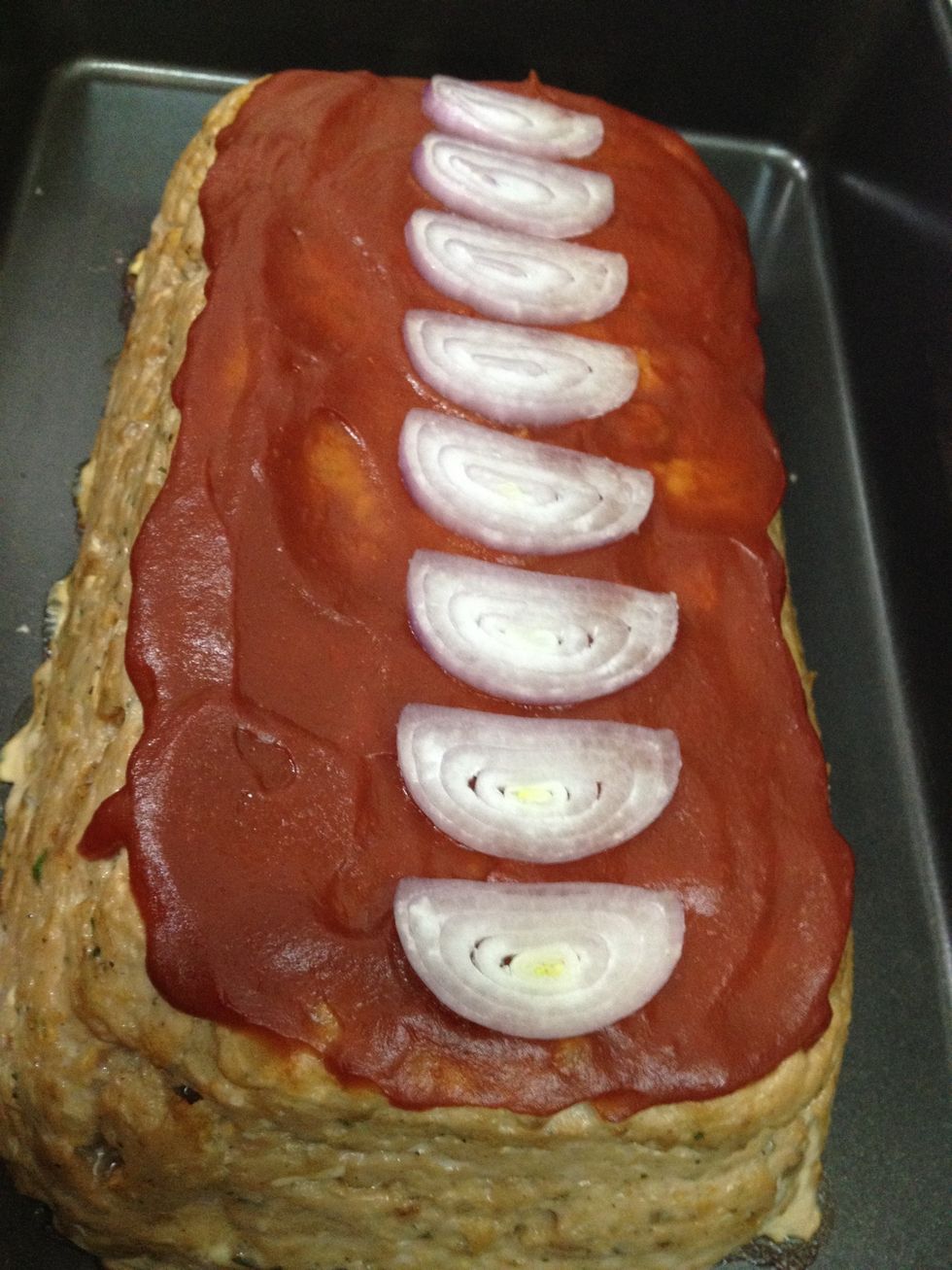 Slice a few shallots to garnish the top of the meatloaf. Place the shallots on top of the ketchup glaze. Then put the pan of meatloaf in a preheated oven to bake for one hour at 325 degrees Farenheit.