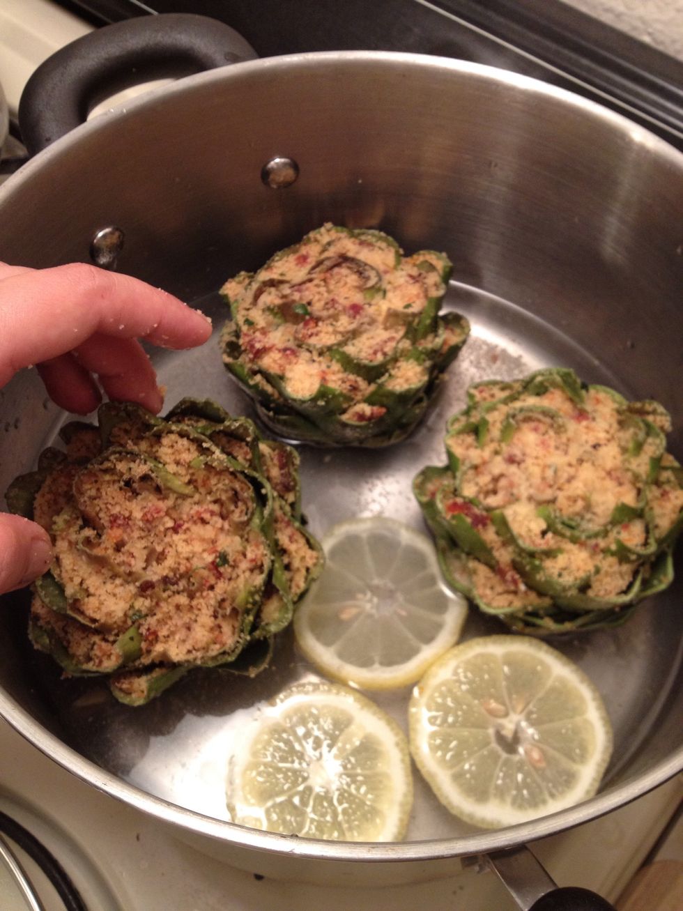 Slice the other half if the lemon and place some slices in a big pot with some water at the bottom. Just enough water to cover the heart of the artichoke. No drowning...