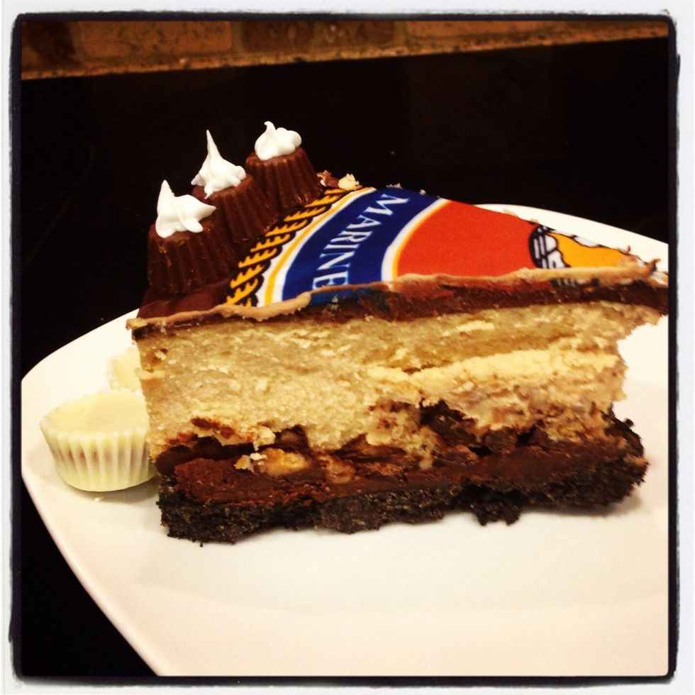 Sliced to show layers. Oreo crust, melted chocolate, chopped Reese's cups, peanut butter cheesecake, melted chocolate.