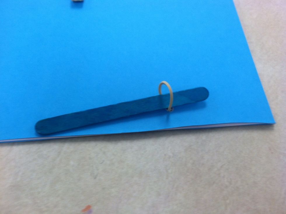 Slide popcicle stick through the ruberband. Cover side. Hold in place.
