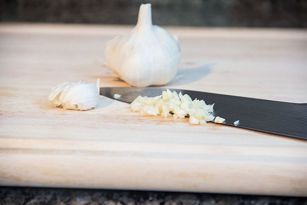 Smash a couple of cloves of garlic with your knife, breaking apart the skin so you can easily peel it off. Then run your knife through the garlic, mincing it up.