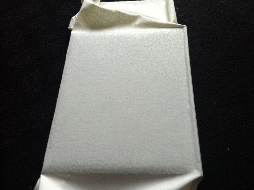 Smooth out from the centre out and fold the excess material under the book cover, repeat for the spine and back cover of book