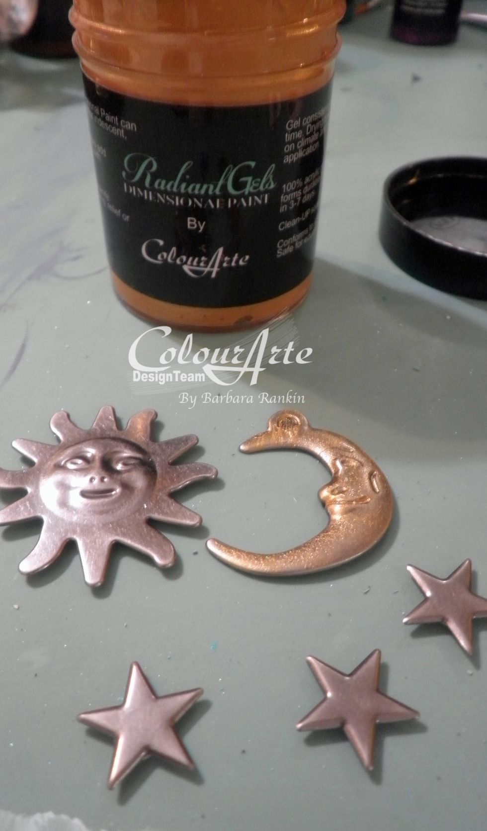 Sponge and dab Emperor\u2019s Gold Radiant Gel onto sun, moon, and stars metal charms. This will give more texture. In the photo, I applied the color to the moon only so you can see the difference.